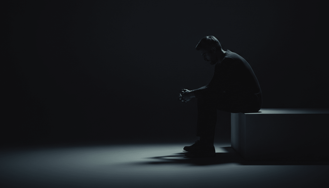 Low-lit image of a tired man sitting alone, symbolizing TestoRise men's vitality and natural hormone support.